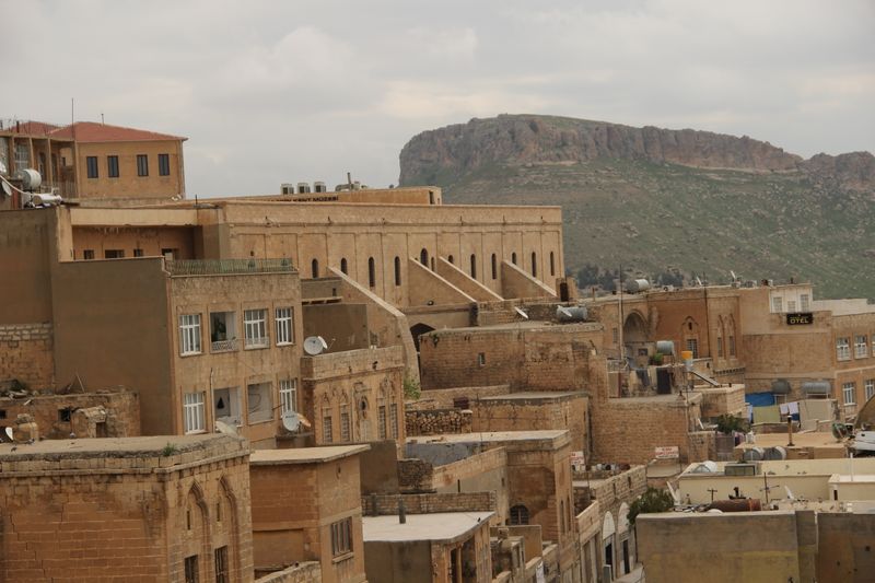 Mardin'in eski şehrinde yamaca sıralanan bal rengi taş evler ve arkada kale sırtı.